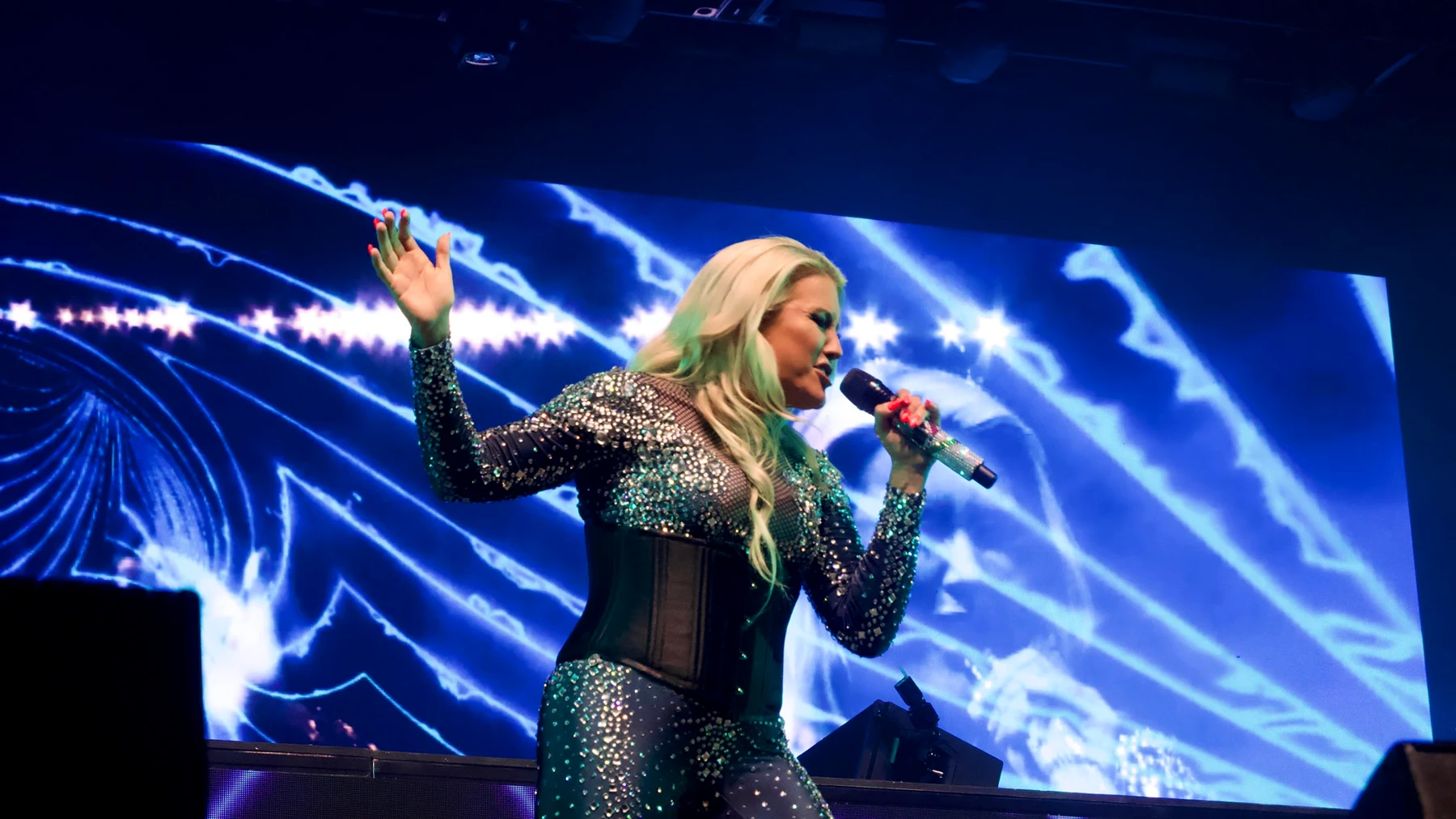Cascada singing live on stage at Motorpoint Arena in a sparkling outfit, in front of a giant blue LED screen