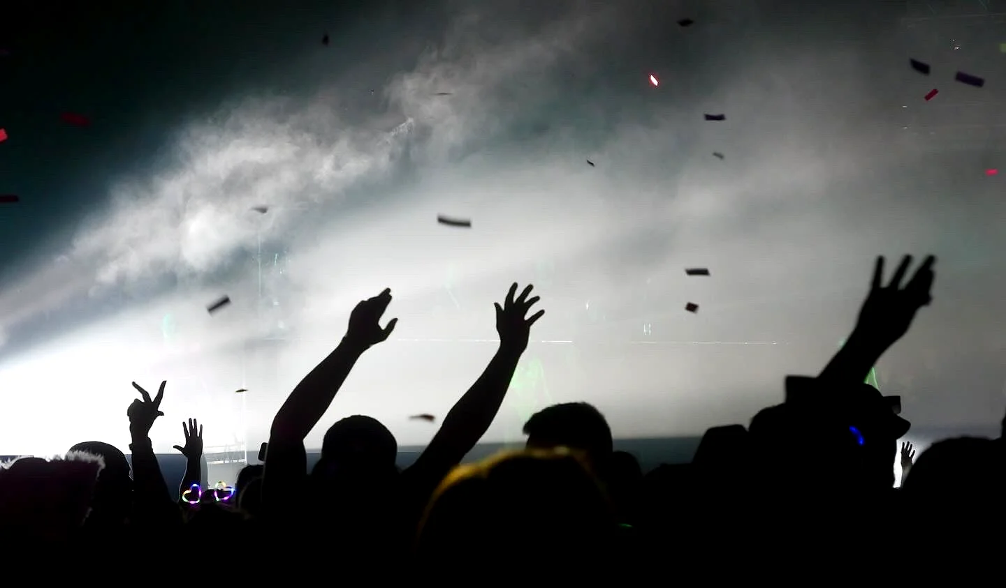 Hands in the air in silhouette as confetti falls through smoky stage light