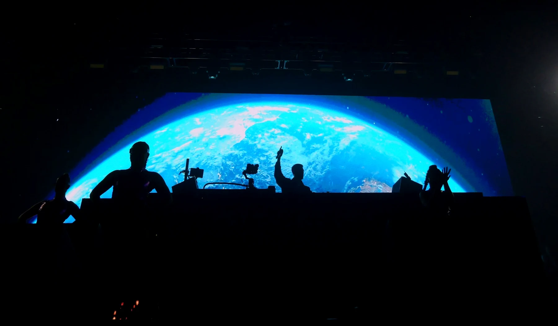 Performers in silhouette in front of a huge screen showing the Earth from space, one arm raised