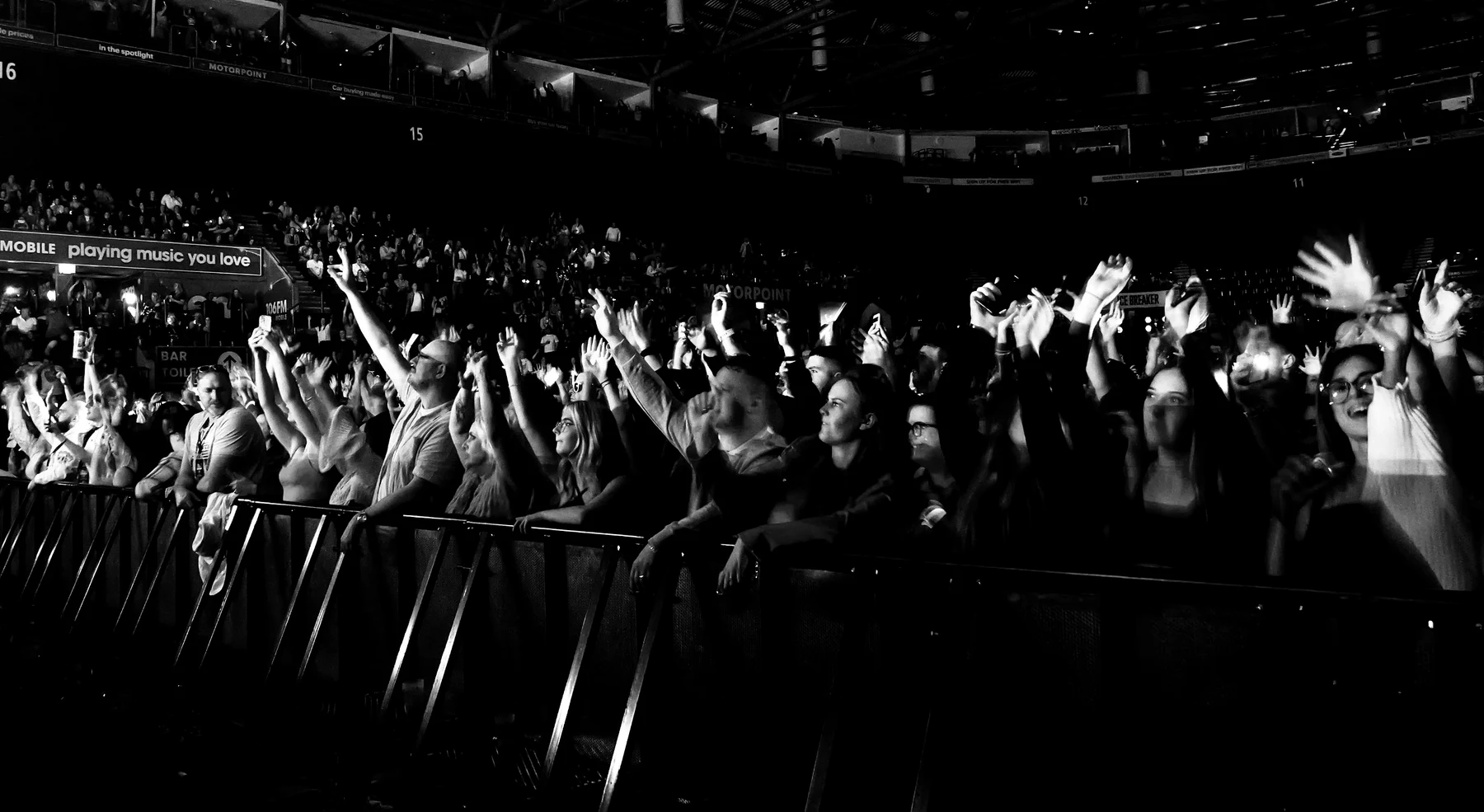 Black and white photograph of the front barrier at Motorpoint Arena, the crowd singing with arms in the air
