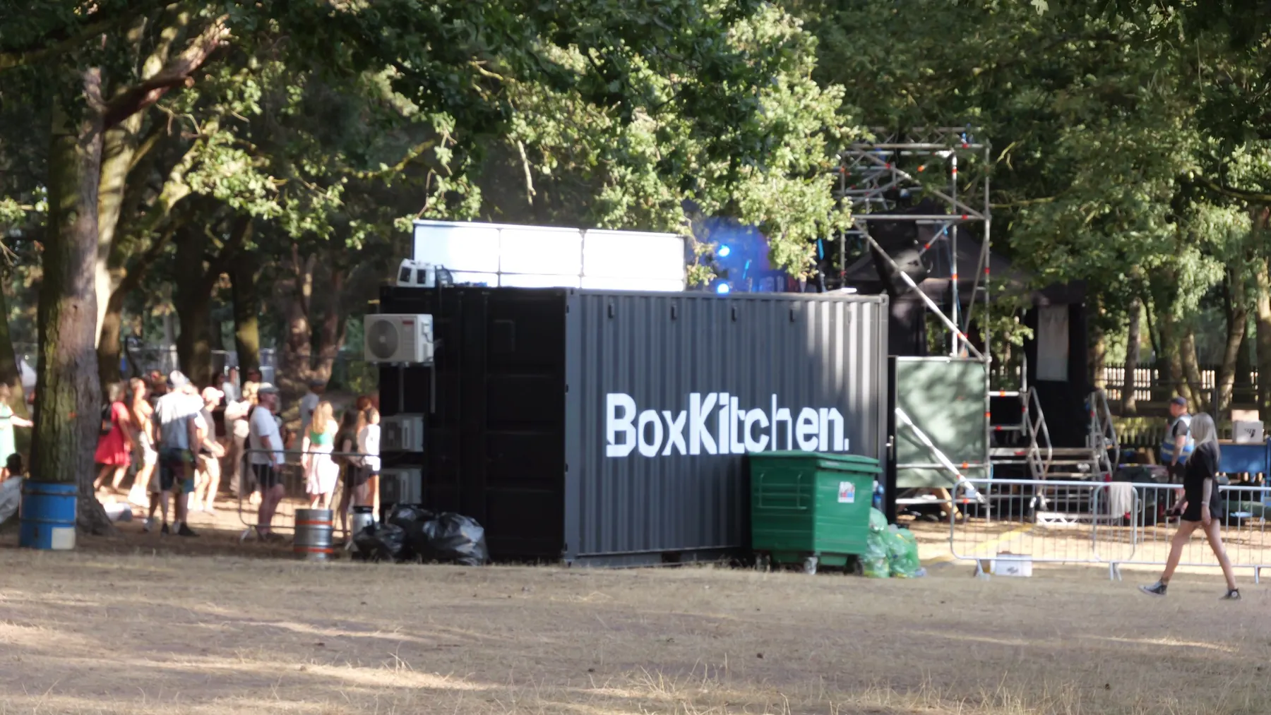 BoxKitchen branded container unit set up in the shade of trees beside a festival stage