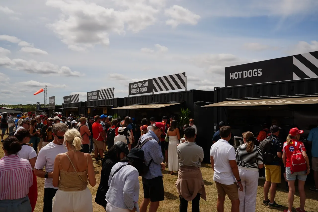 Crowds queuing at a row of black street food container units with diagonal stripe fascias at the Silverstone Grand Prix