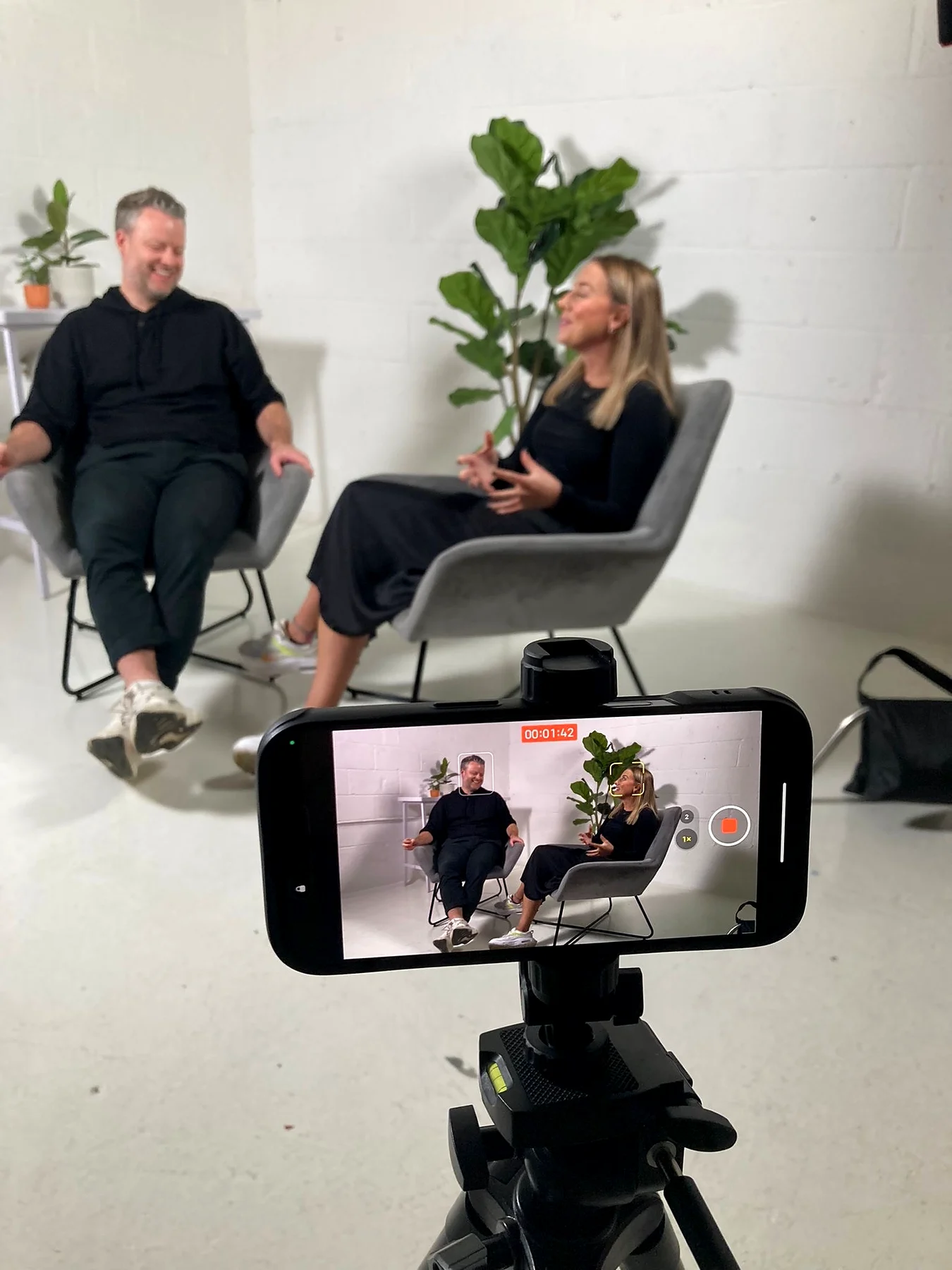 The Project Inc interview framed on a phone monitor in the foreground, with the two speakers sat in the studio behind