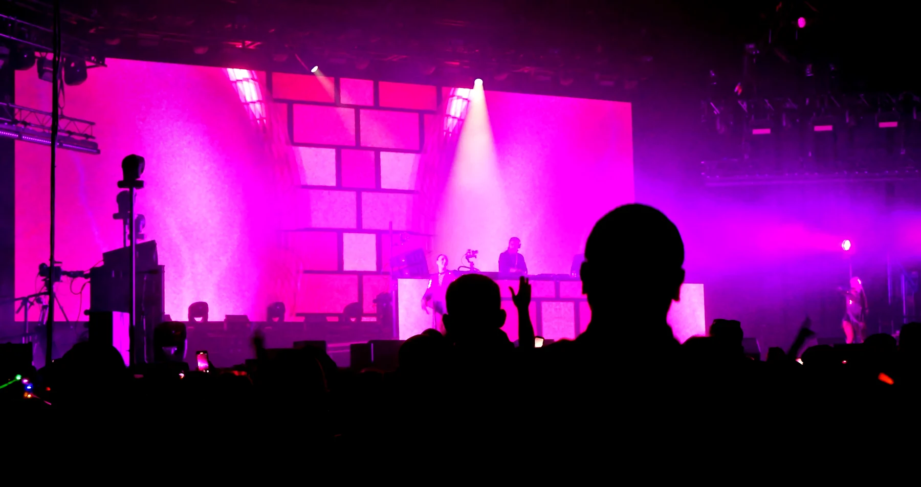 Stage washed in hot pink with a brick-pattern LED wall, the crowd in silhouette in front