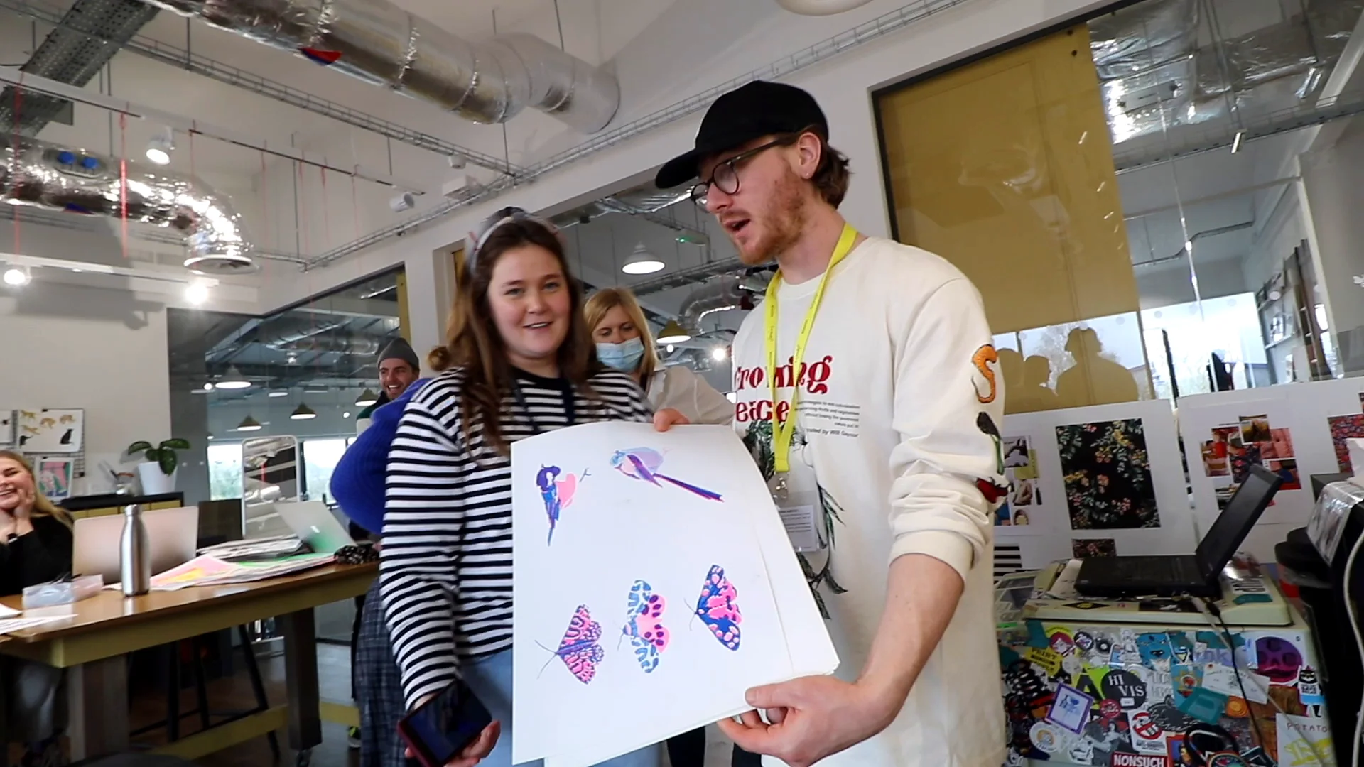 A host in a cap shows the team a sheet of pink and purple printed motifs