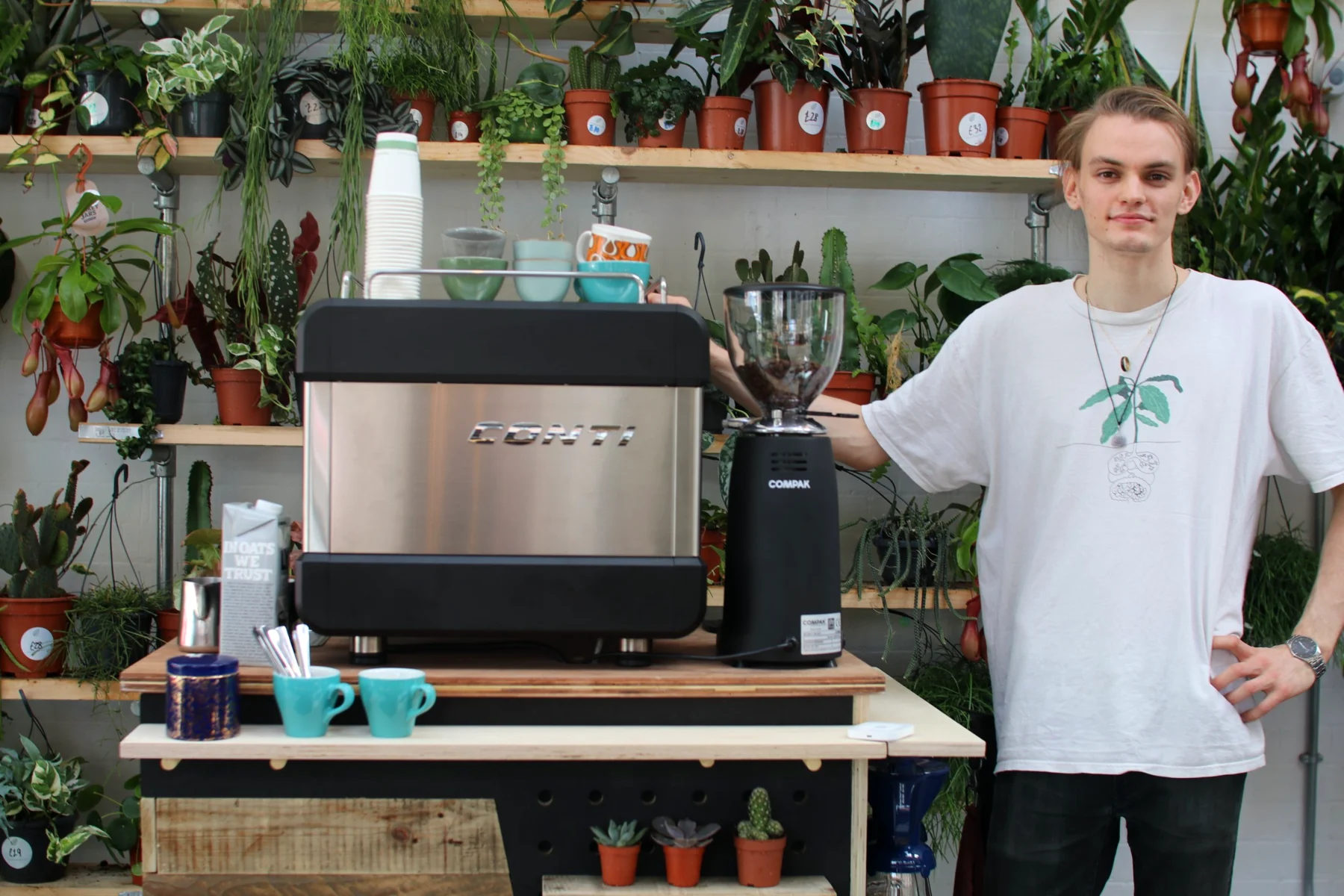 The Lono Espresso barista standing beside the coffee cart with a Conti espresso machine and Compak grinder, teal cups on the counter