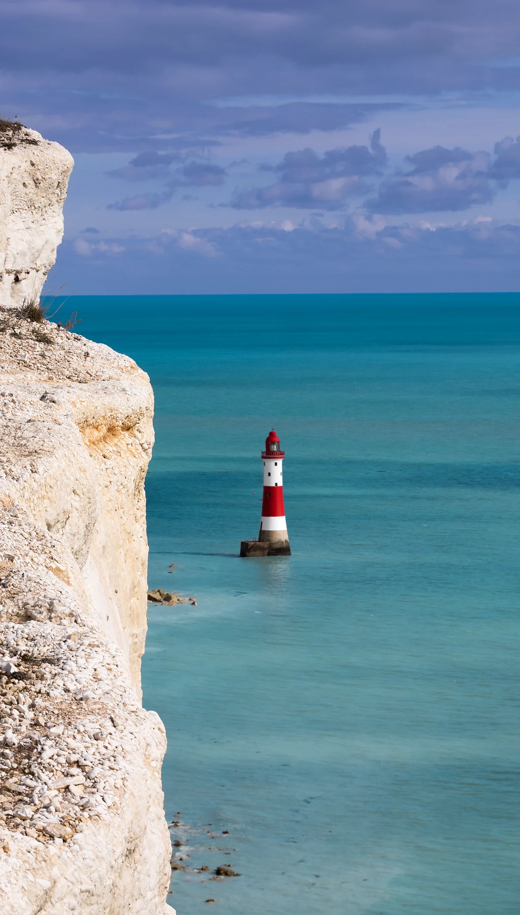Red and white Beachy Head lighthouse in a turquoise sea at the foot of white chalk cliffs