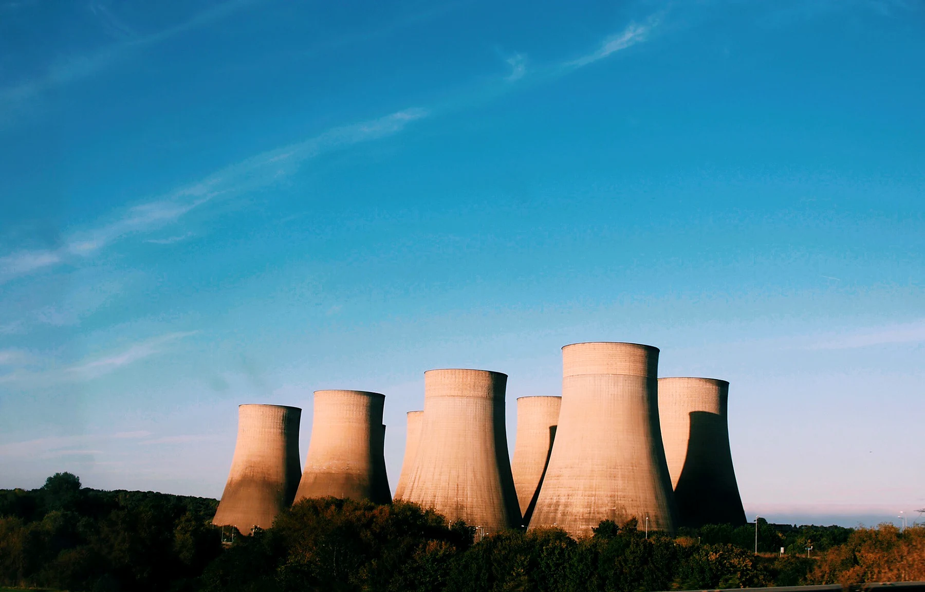 Power station cooling towers near Nottingham lit warm by low evening sun under a deep blue sky with wispy cloud