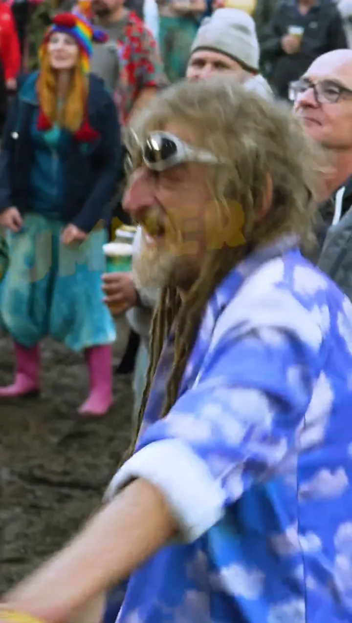 A festival goer in a cloud print shirt and goggles dancing in the mud at Solfest