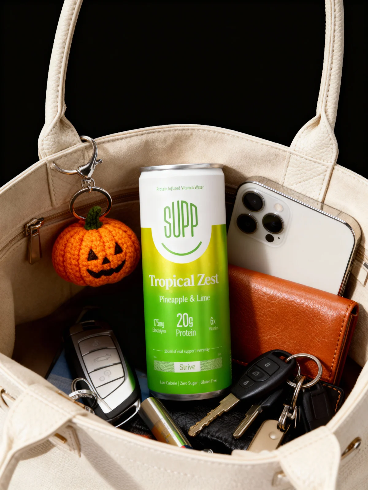 A tote bag with a Supp can, a crochet pumpkin, a phone, keys and a purse inside