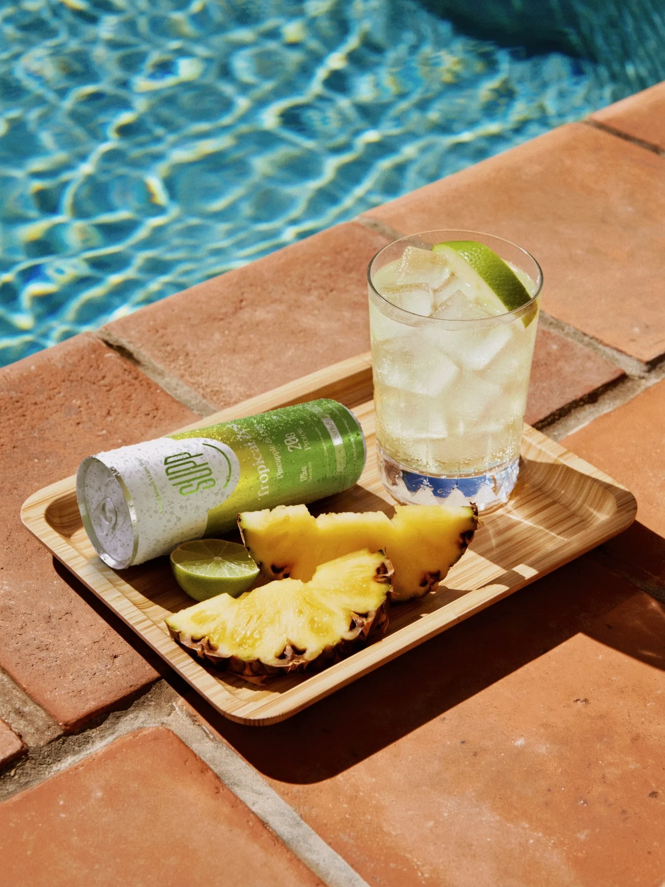 Supp Tropical Zest can on a wooden tray by a sparkling pool, with pineapple slices and a glass of ice and lime