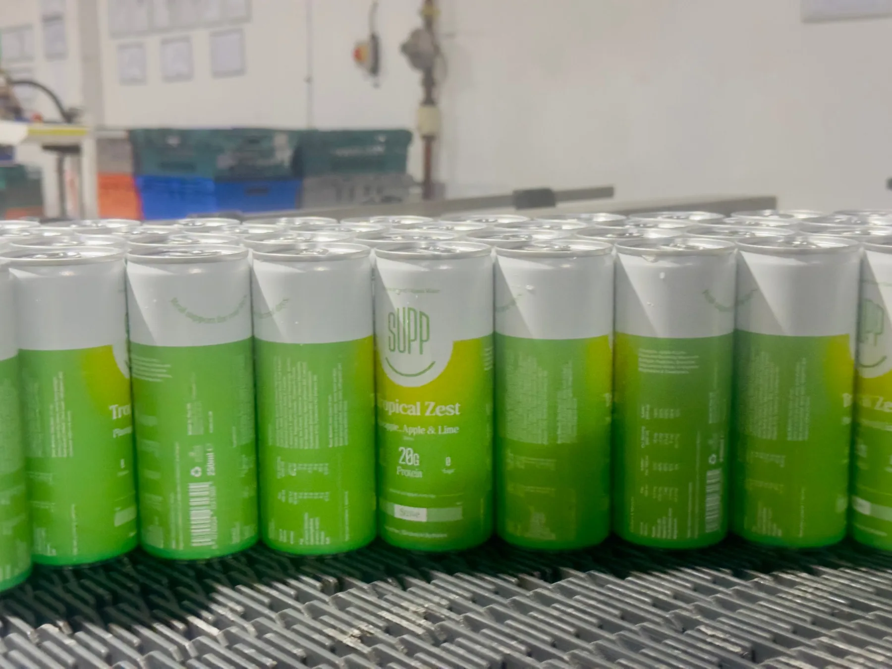 Row of green and white Supp Tropical Zest cans with 20g protein moving along the conveyor