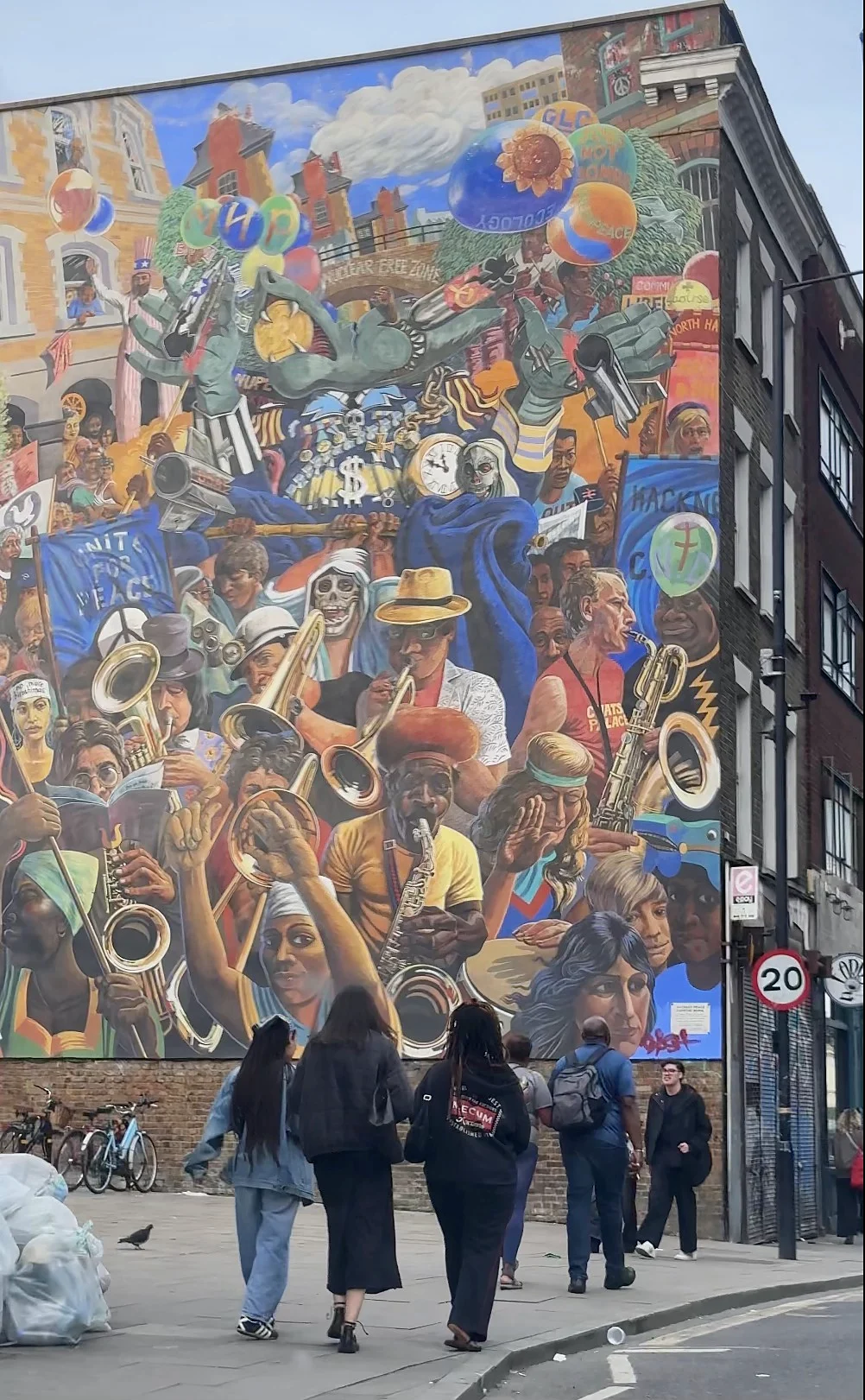 A huge colourful street mural of musicians covering the side of a London building, with people walking past