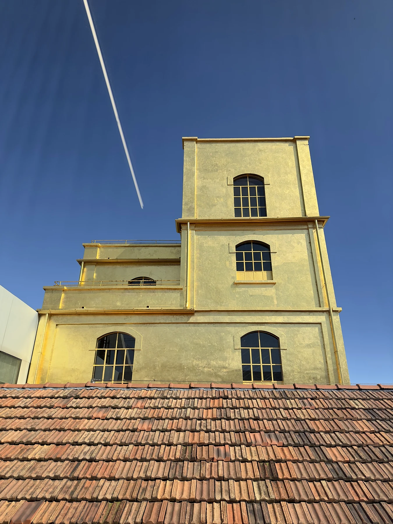 The gold leaf clad tower at Fondazione Prada in Milan above a terracotta roof, with a vapour trail across the blue sky