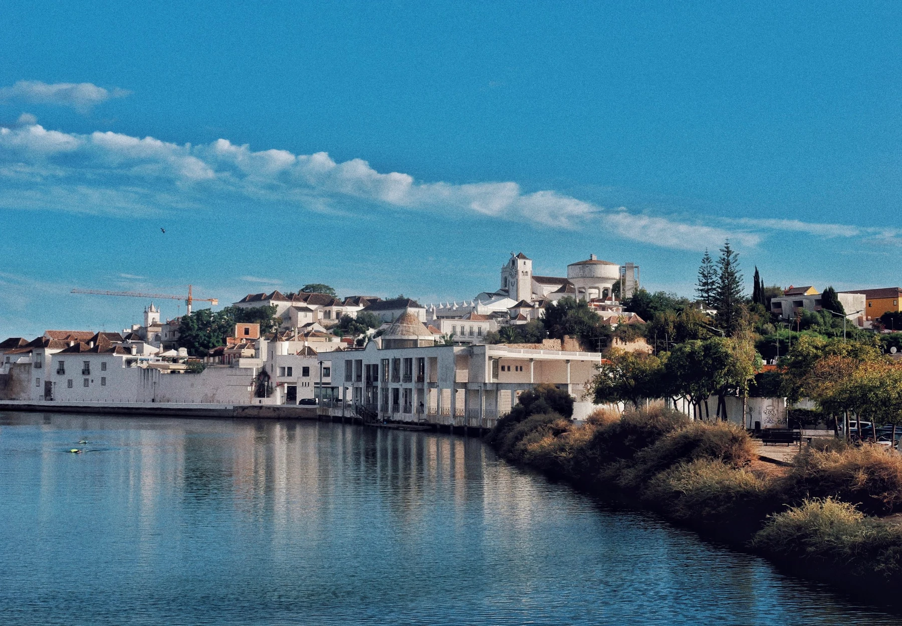 The whitewashed old town of Tavira in Portugal rising above the river under a deep blue sky, reflected in the water