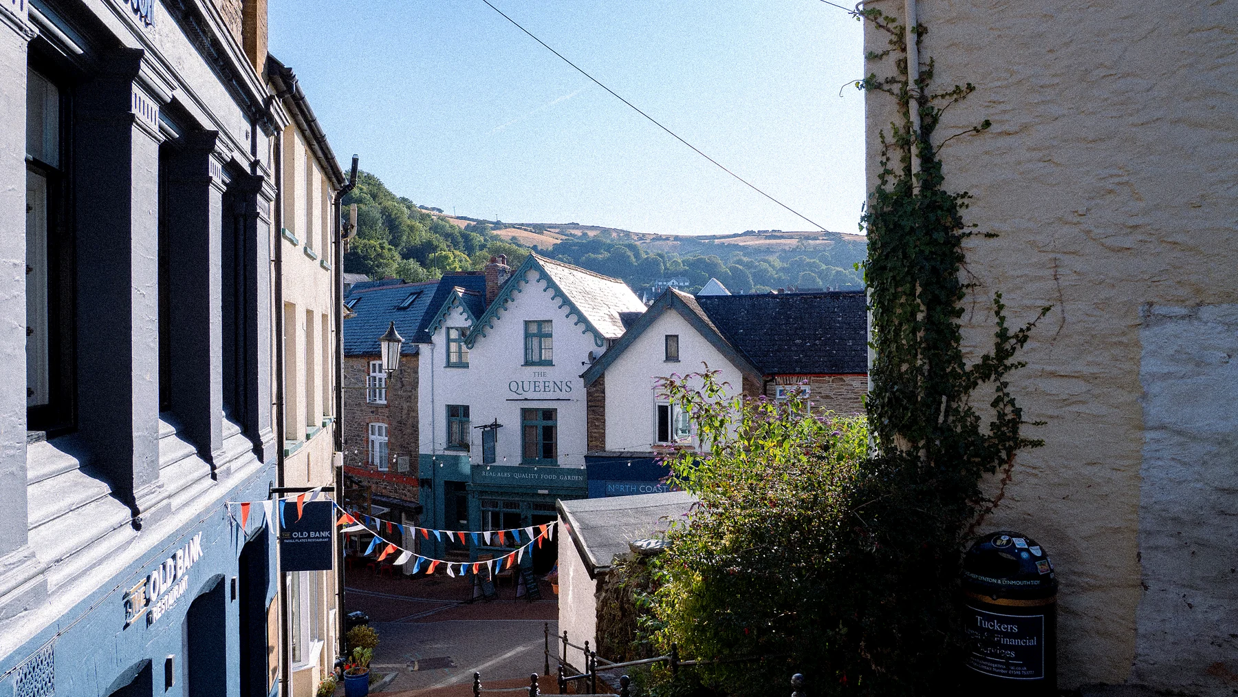 A narrow village street with whitewashed houses, bunting and climbing plants in the summer sun